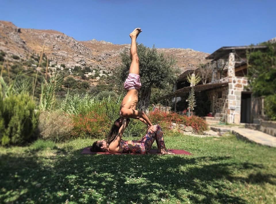 Karakaya Retreat'in bahçesinde acro-yoga: base ellerini yukarı uzatmış, üstteki kişi baş aşağı, bacakları gökyüzüne dik