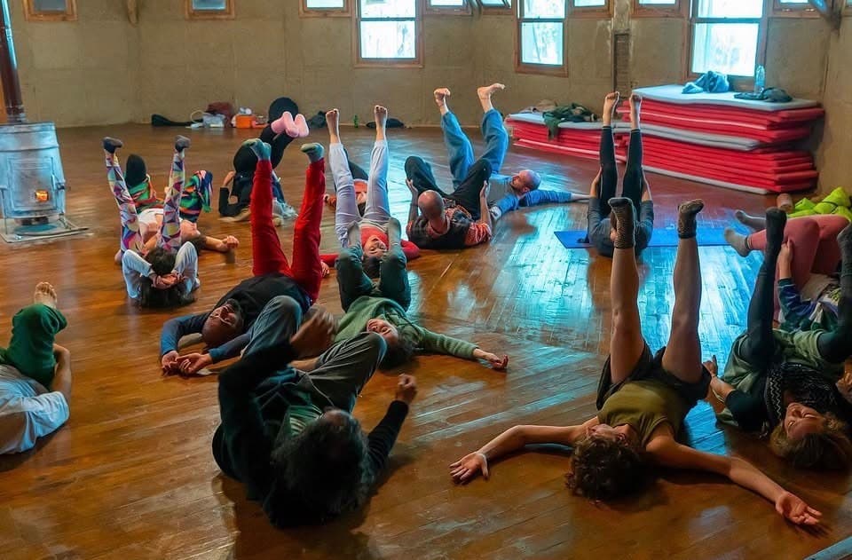 Ahşap zeminde sırtüstü uzanıp bacaklarını havaya kaldıran katılımcılar