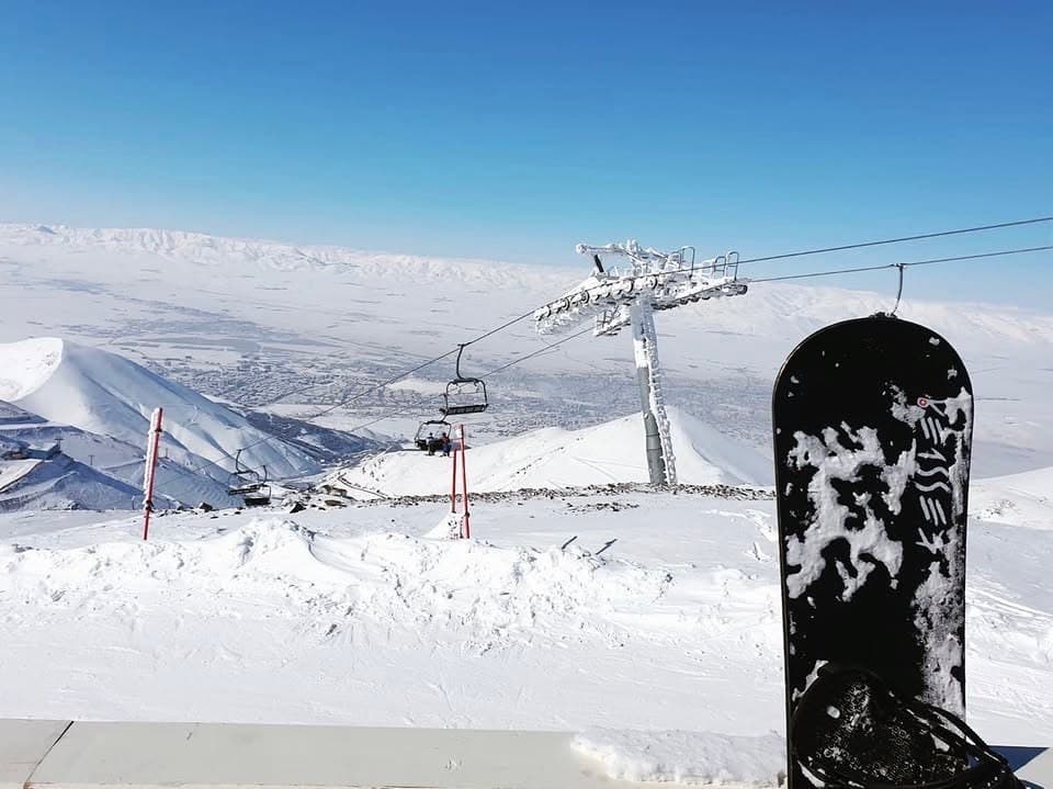 Dağın tepesinden telesiyej hattı ve karlı vadi manzarası, önde bir snowboard
