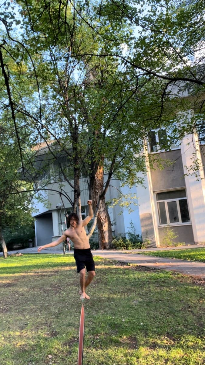 Türker bahçede, ağaçların altında slackline üzerinde dengede