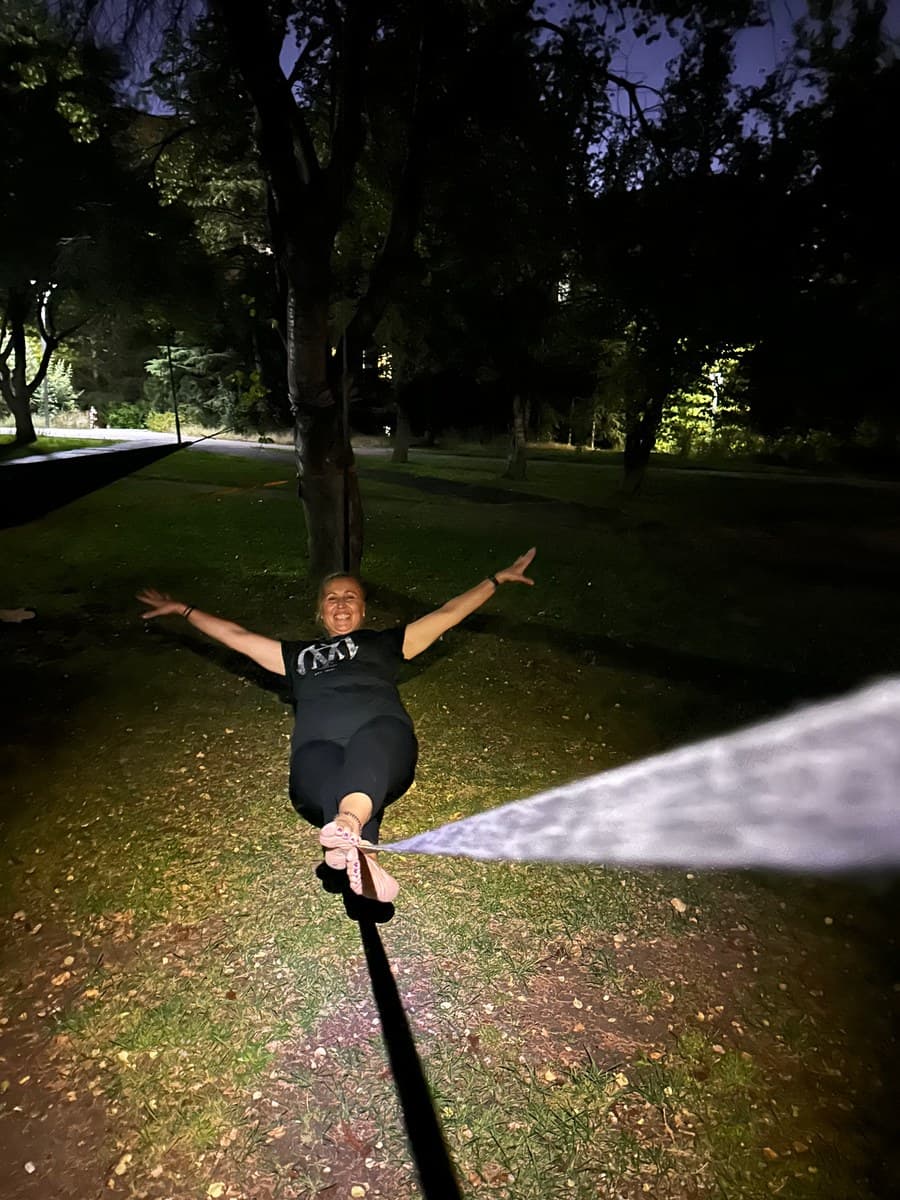 Gece, parkta slackline üzerinde kollarını açmış gülümseyen bir kadın